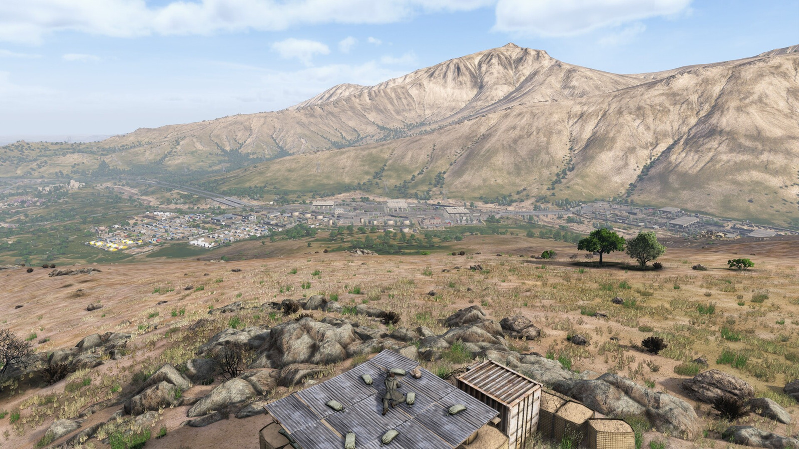 DayZ Badlandsのナスダラ州。乾燥した山々の麓に集落と道路が広がり、手前の屋根に生存者がいる。